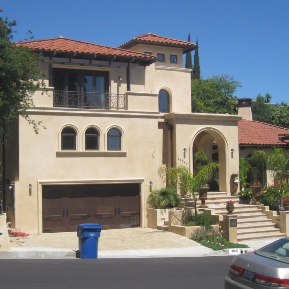 A large beige Mediterranean-style house with red tile roof and arched windows.