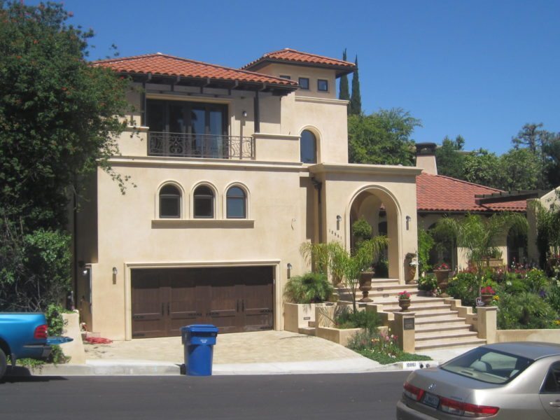A large beige Mediterranean-style house with red tile roof and arched windows.