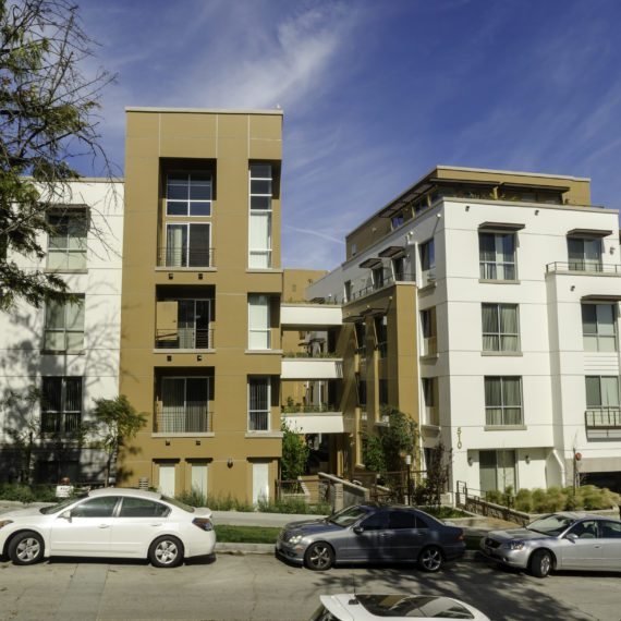 Two residential buildings with parked cars in front under a partly cloudy sky.