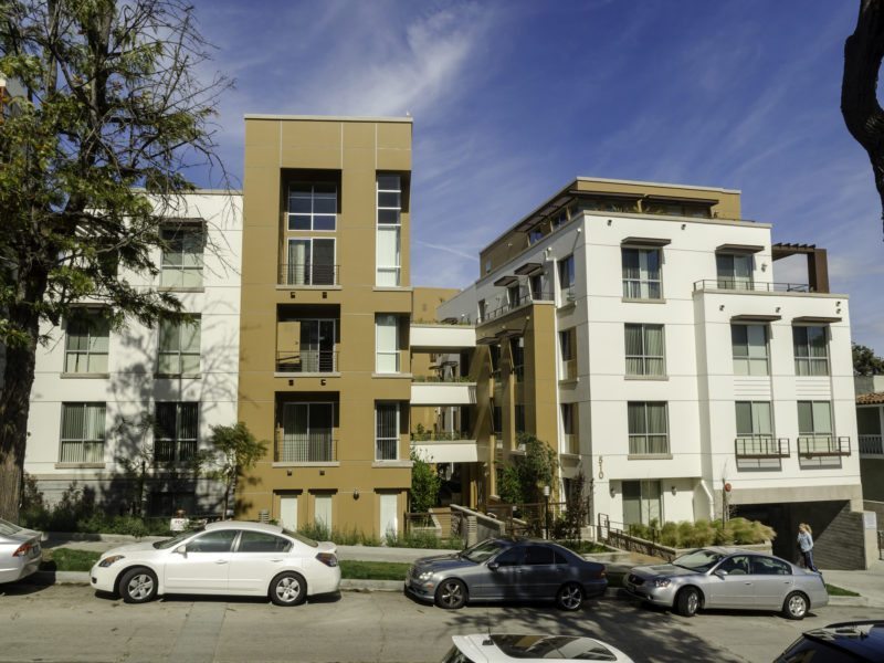 Two residential buildings with parked cars in front under a partly cloudy sky.