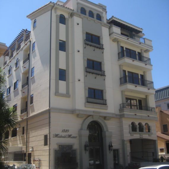A multi-story beige building with balconies and arched entrance under clear blue sky.