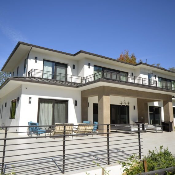 Modern two-story house with large windows and balcony under clear blue sky.