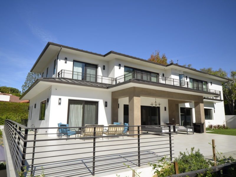 Modern two-story house with large windows and balcony under clear blue sky.
