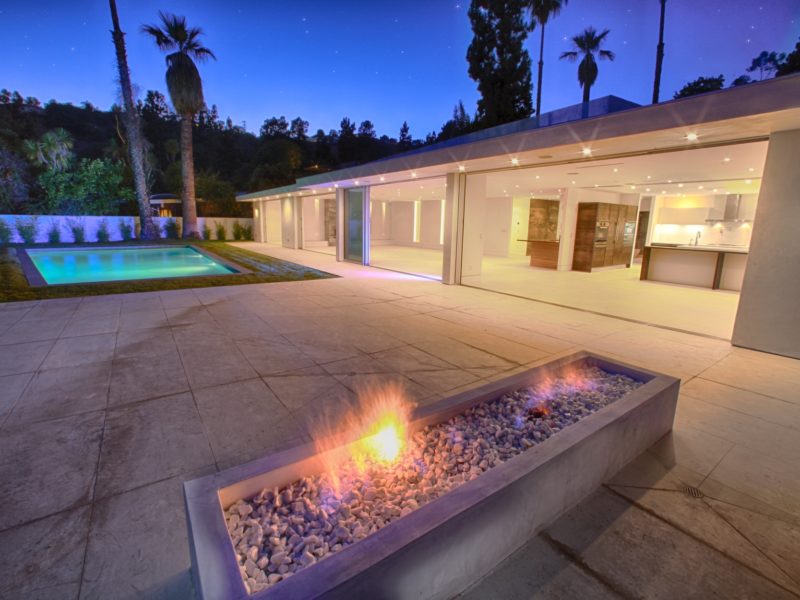 Modern backyard with a fire pit and pool at dusk.