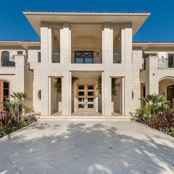 Modern beige house entrance with large pillars and clear blue sky.