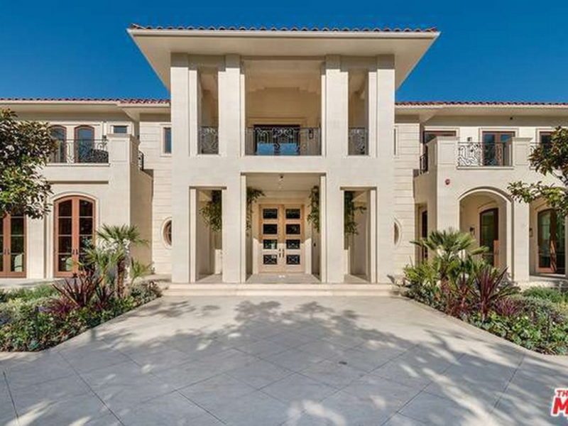 Modern beige house entrance with large pillars and clear blue sky.