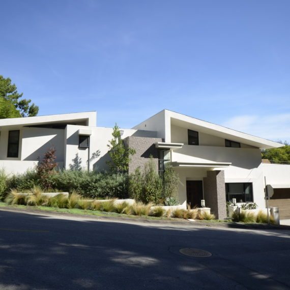 Modern white house with angular design and greenery in front.