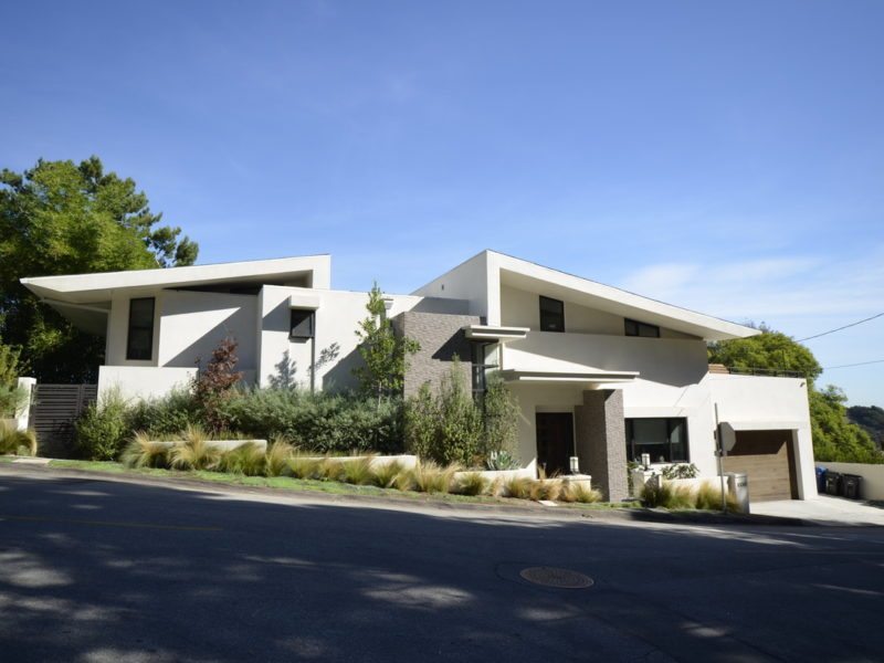 Modern white house with angular design and greenery in front.