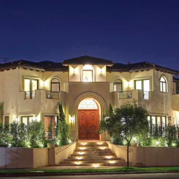 Luxurious mansion illuminated at night with a grand entrance and landscaped garden.