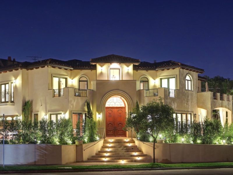 Luxurious mansion illuminated at night with a grand entrance and landscaped garden.
