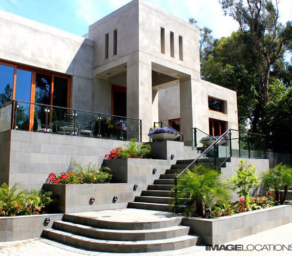 Modern stone house with large windows and a grand staircase.