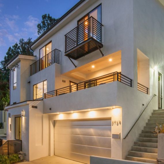 Modern multi-story house with balcony and garage illuminated at dusk.