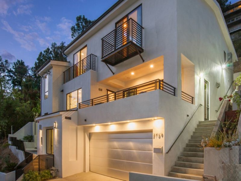 Modern multi-story house with balcony and garage illuminated at dusk.