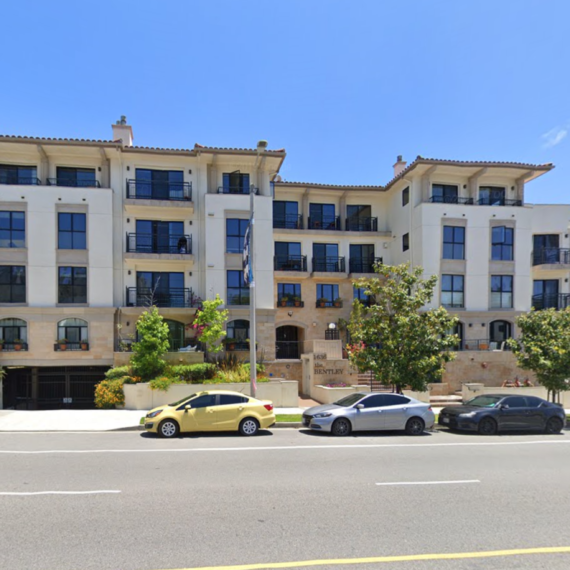 Modern apartment building with parked cars in front on a sunny day.