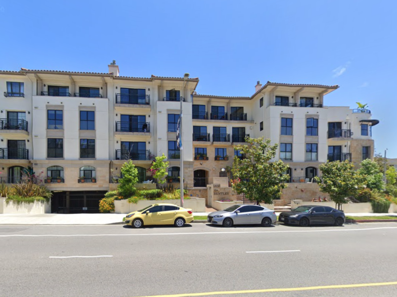 Modern apartment building with parked cars in front on a sunny day.