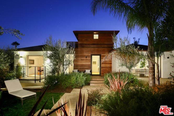 Modern house with warm lighting and landscaped garden at night.