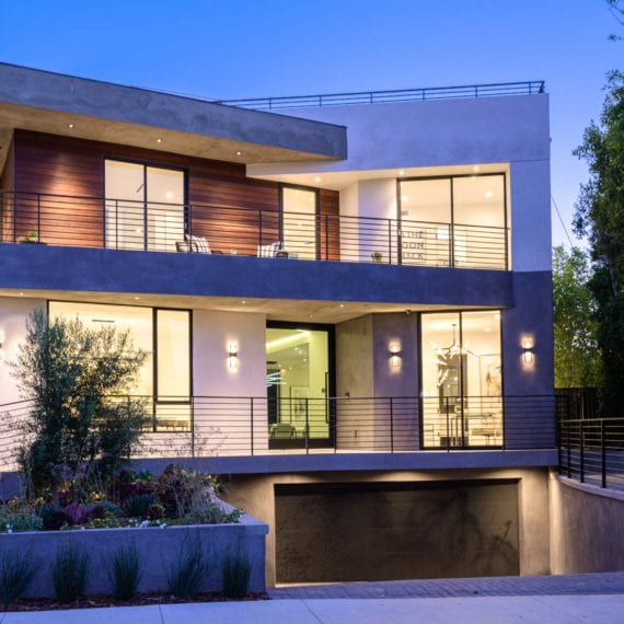 Modern two-story house with large windows and warm lighting at dusk.