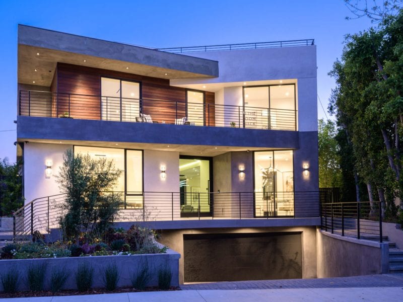Modern two-story house with large windows and warm lighting at dusk.