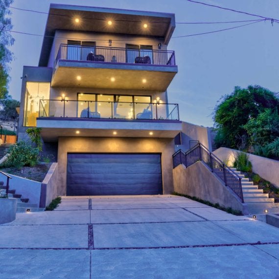 Modern three-story house with large windows and warm exterior lighting at dusk.