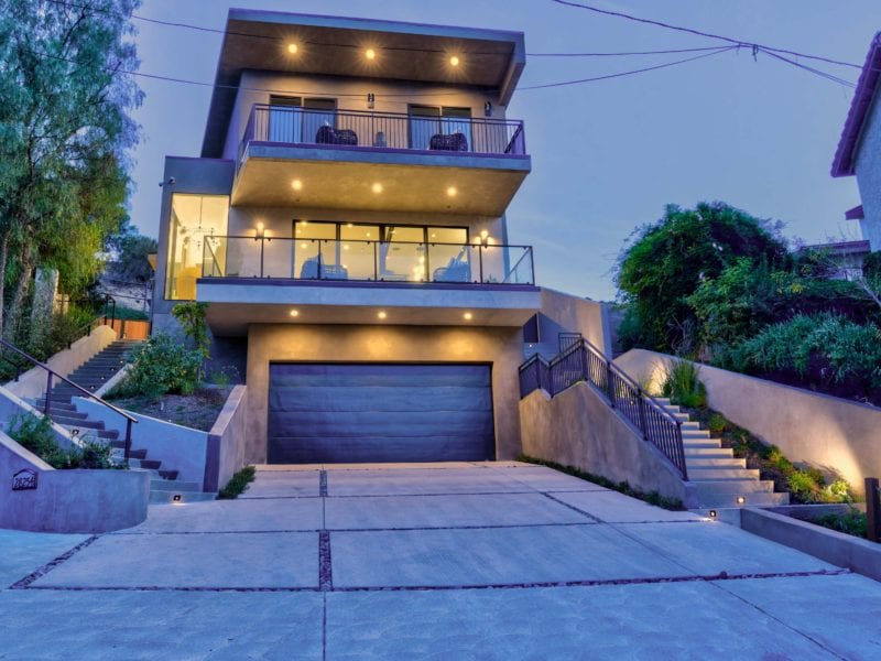 Modern three-story house with large windows and warm exterior lighting at dusk.