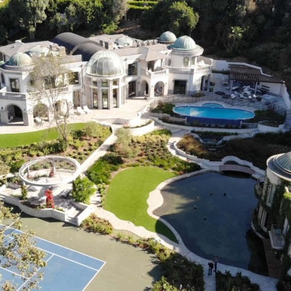 Luxurious mansion with pools and sports courts surrounded by greenery.
