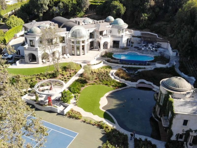 Luxurious mansion with pools and sports courts surrounded by greenery.