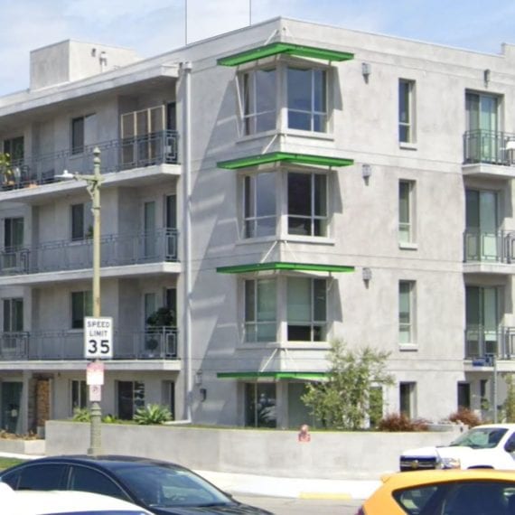 Modern multi-story apartment building with balconies and parked cars outside.