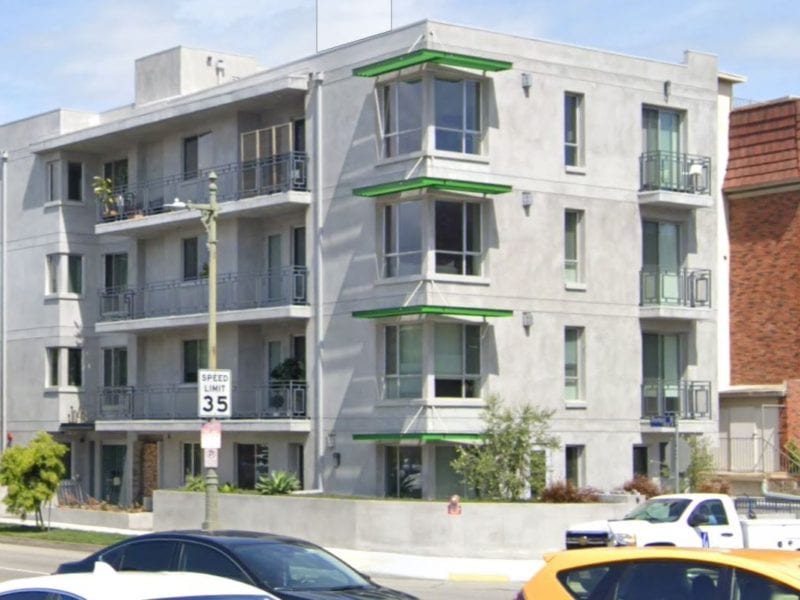 Modern multi-story apartment building with balconies and parked cars outside.