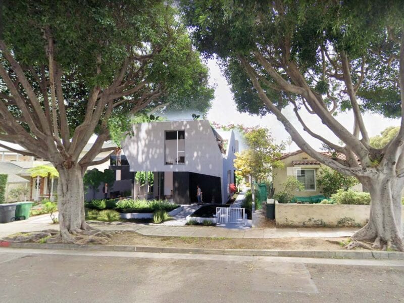 Modern house under large trees on a sunny day.