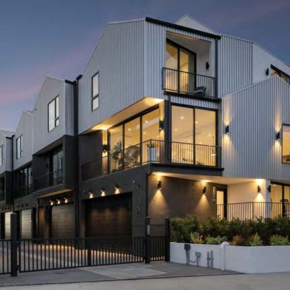 Modern multi-story house with large windows and warm lighting at dusk.
