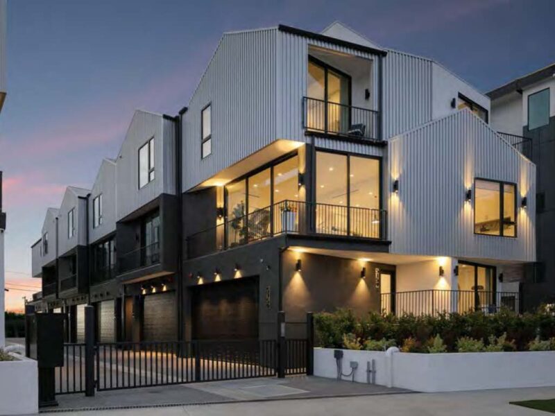 Modern multi-story house with large windows and warm lighting at dusk.